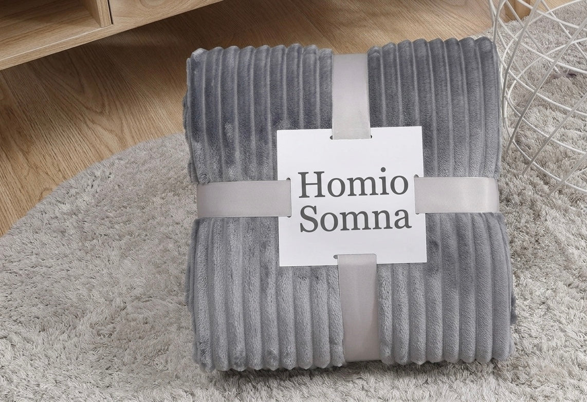 Folded gray blanket with 'Homio Somna' label on a light wooden floor.