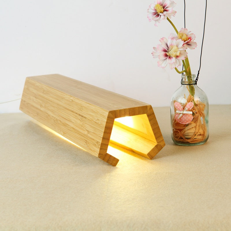 Wooden lamp with a warm glow on a beige surface, next to a vase with flowers.