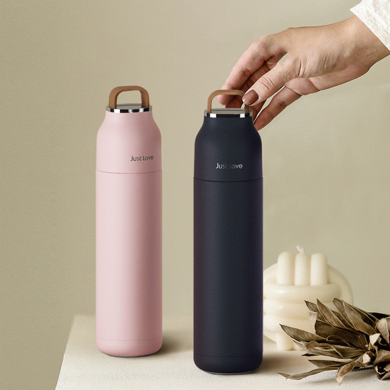 Two insulated bottles, one pink and one navy, with a hand holding the navy bottle against a neutral background.