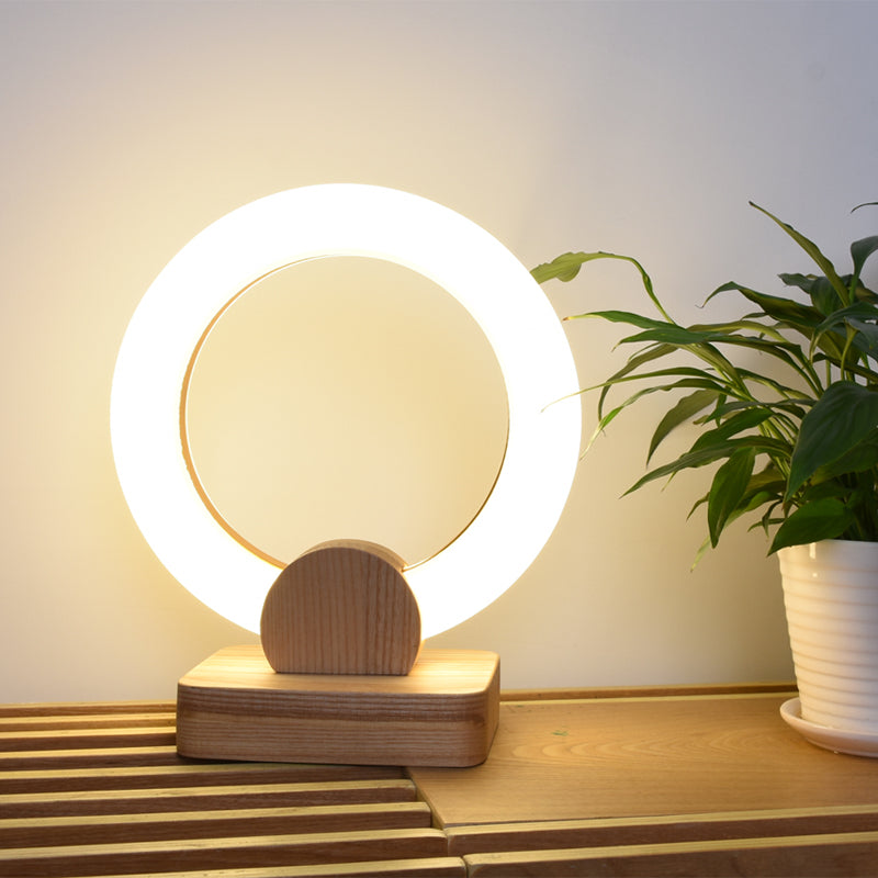 Wooden table lamp with circular design on a wooden surface next to a plant