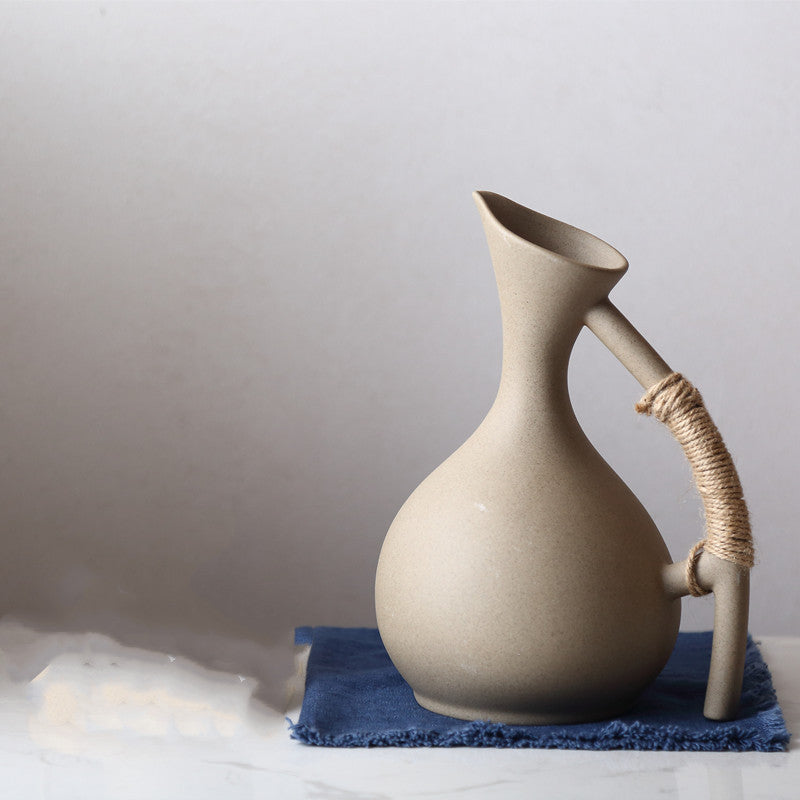 Beige ceramic pitcher with a handle on a blue cloth against a light gray background