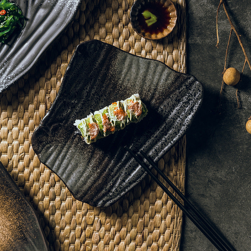Sushi roll on a black textured plate with chopsticks on a woven mat