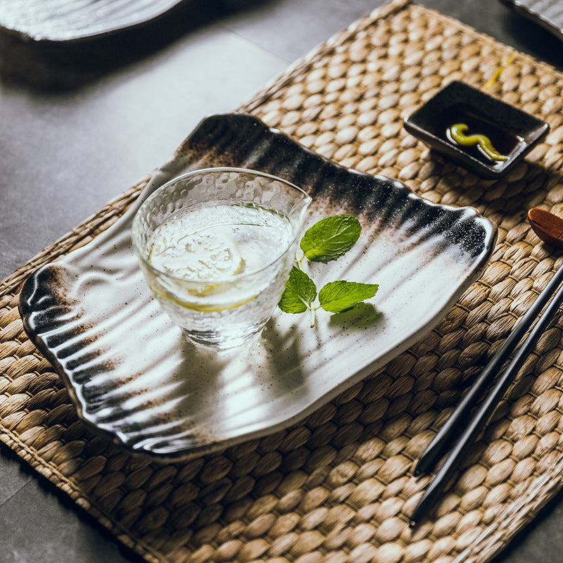 Glass of water with mint leaves on a decorative plate with chopsticks and a small dish on a woven mat.