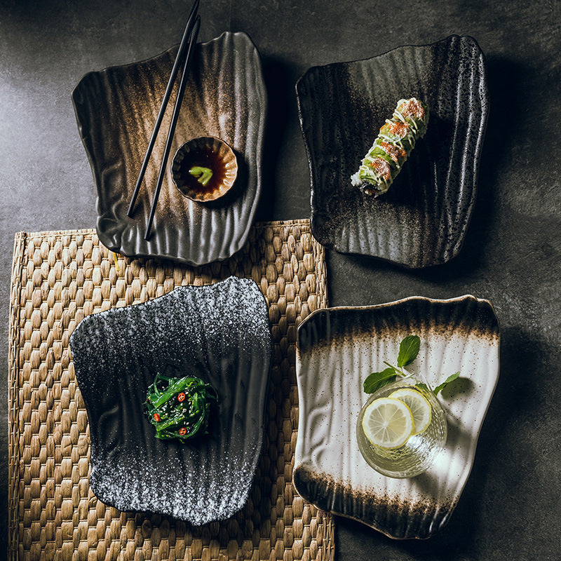 Four square ceramic plates with textured edges, each containing different food items on a dark surface.