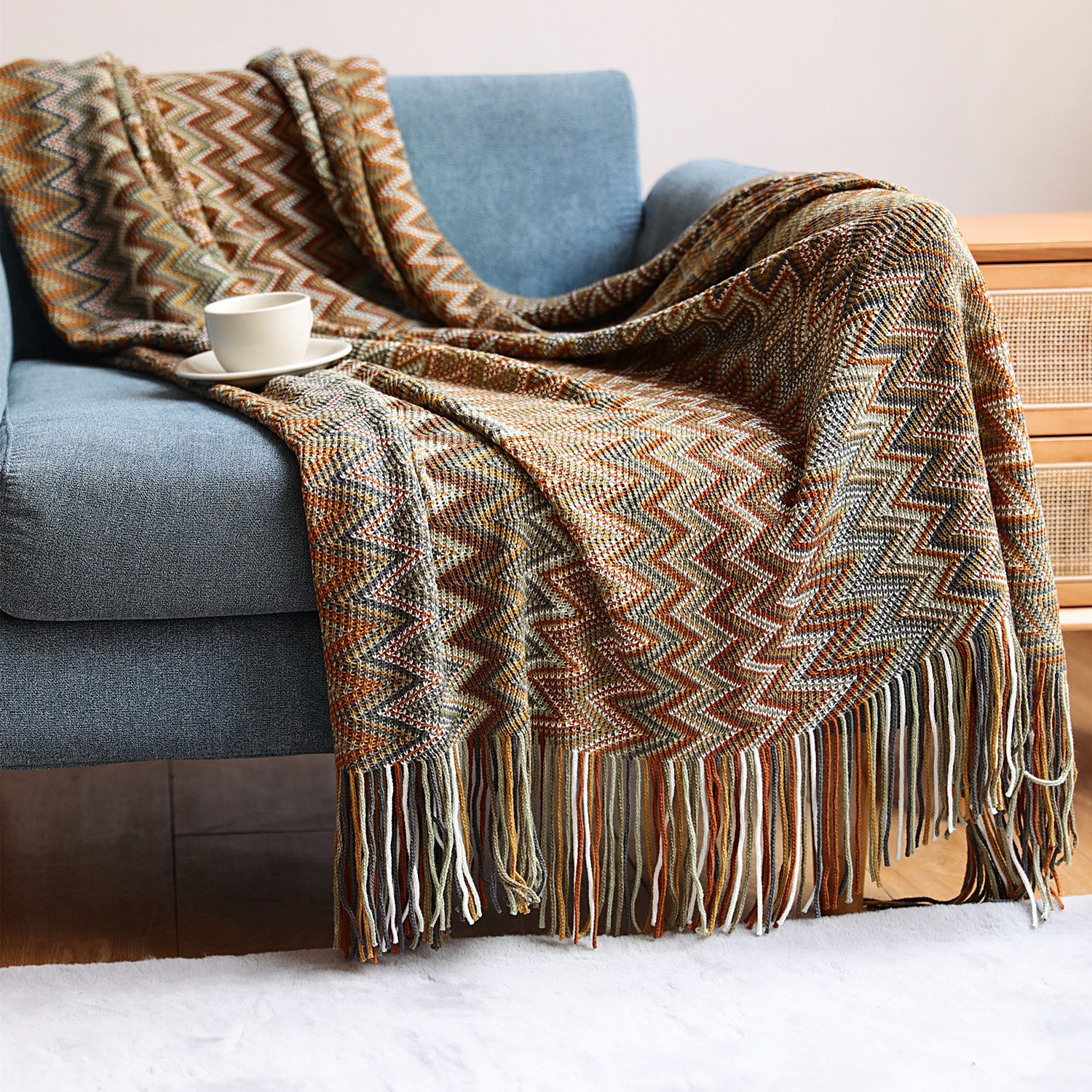 Woven blanket with fringes draped over a blue sofa with a cup of coffee on a white surface.