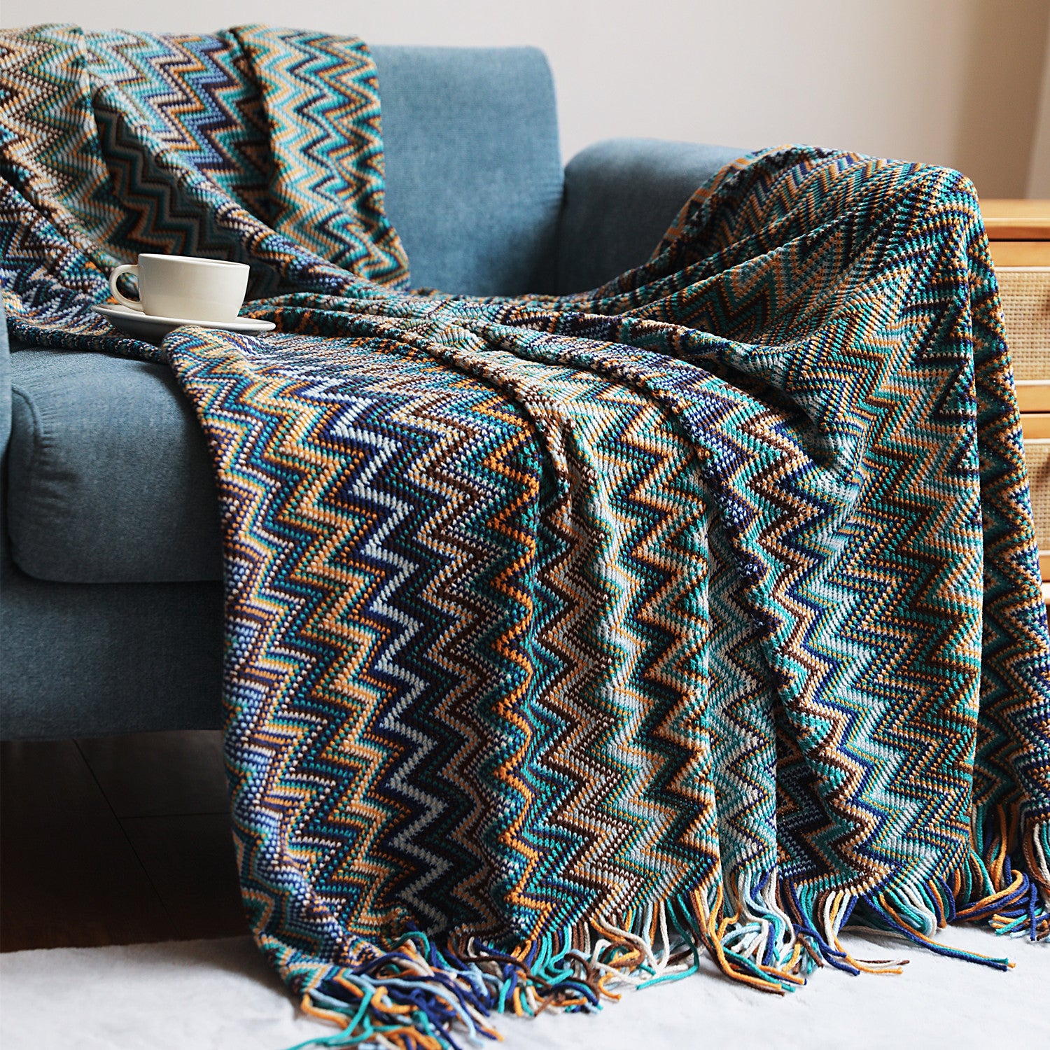 Patterned blanket draped over a blue armchair with a cup on a small table.