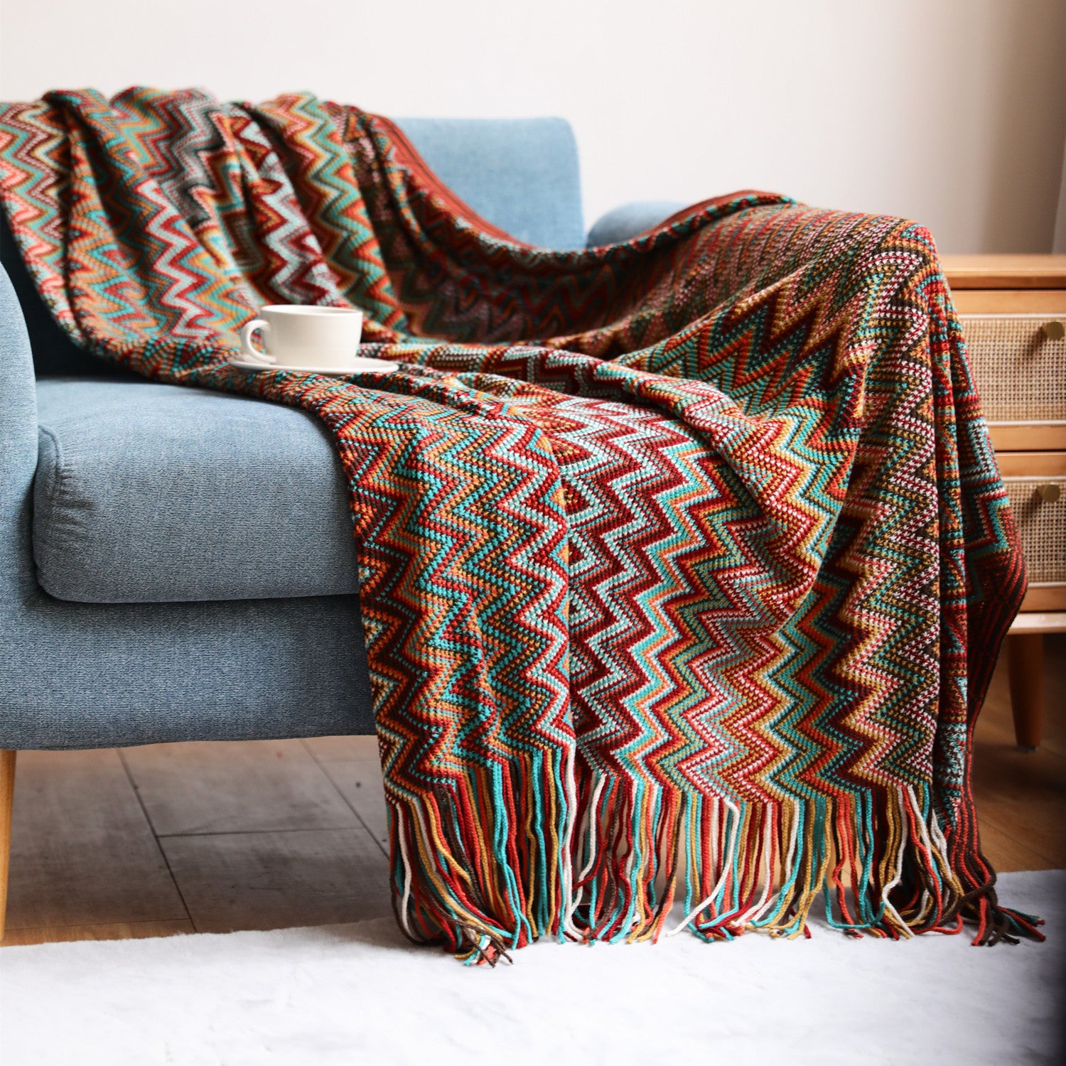 Colorful zigzag patterned blanket draped over a blue sofa with a cup on it, in a cozy living room setting.