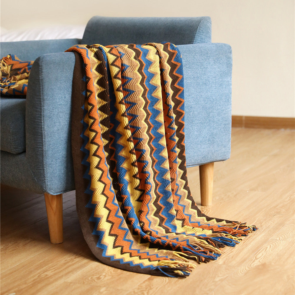 Colorful zigzag patterned blanket draped over a blue armchair on a wooden floor.