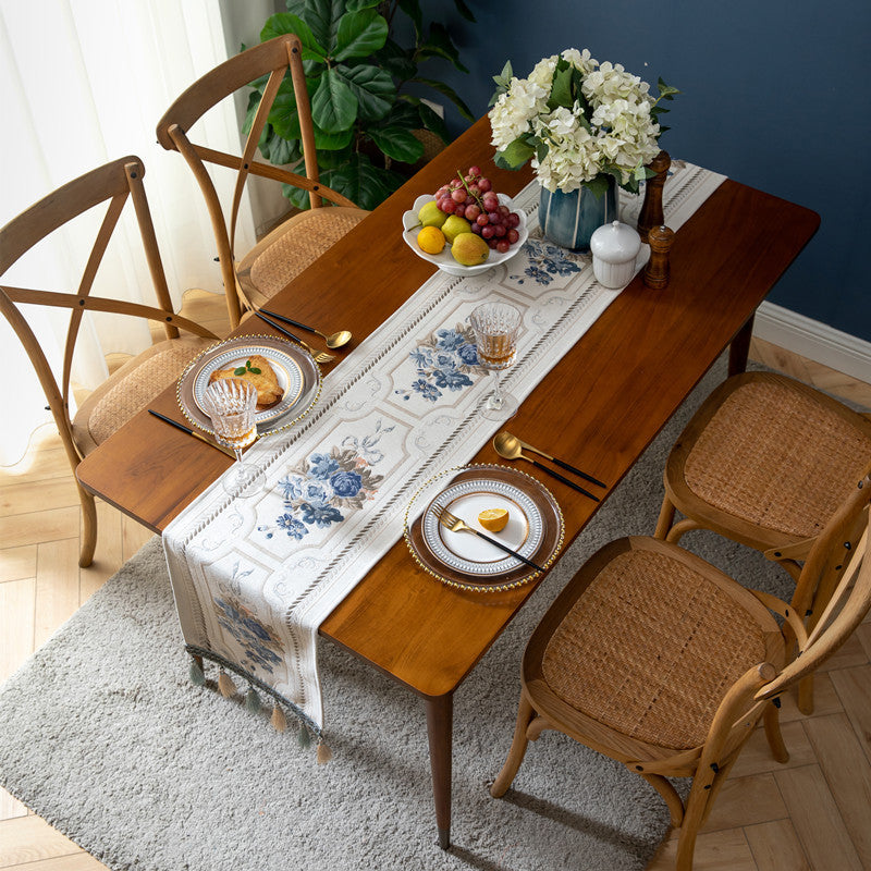 Dining table set with a floral table runner, plates, and chairs in a room with a blue wall.
