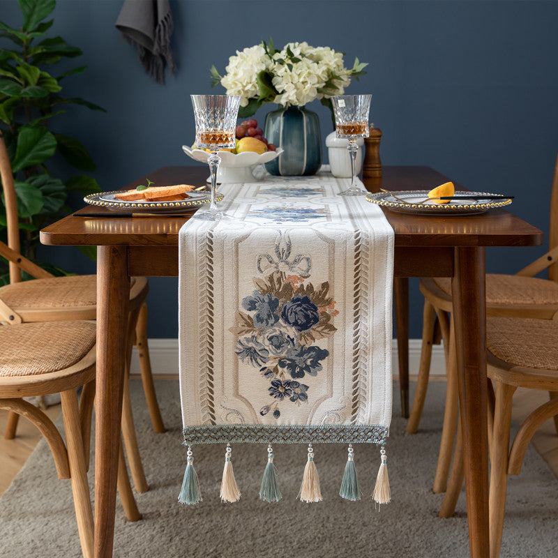 Dining table set with a decorative table runner, glasses, and fruit against a blue wall.