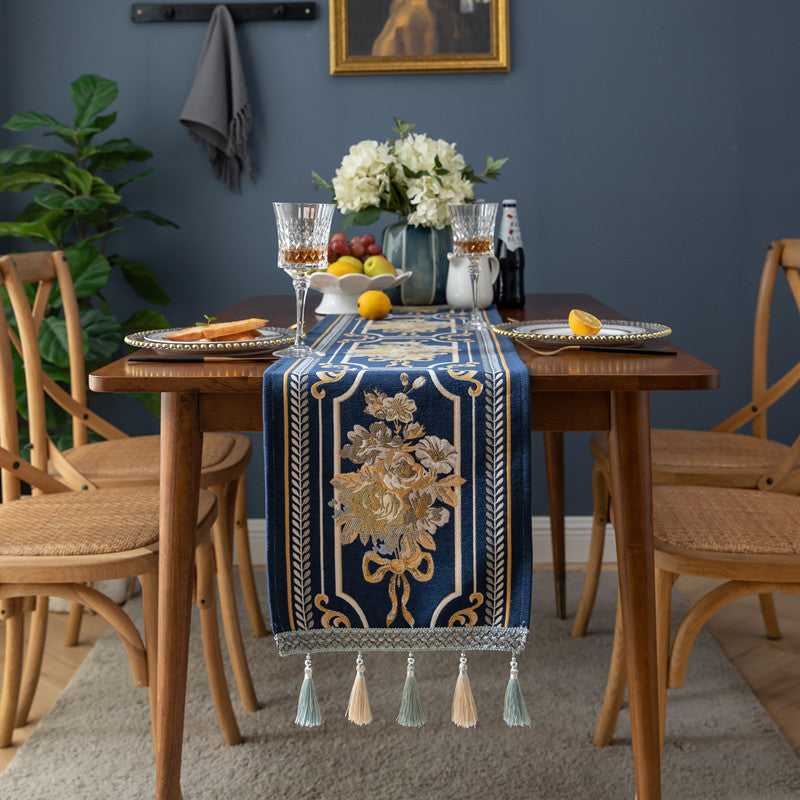 Dining table set with a decorative blue and gold table runner, glasses, and fruit against a blue wall.