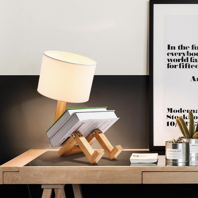 Wooden lamp stand with books and a lamp on a wooden surface, with a framed picture in the background.