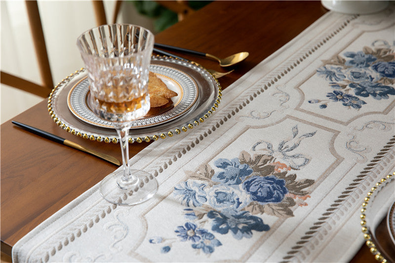 Table setting with floral table runner, glass, and cutlery on a wooden table.
