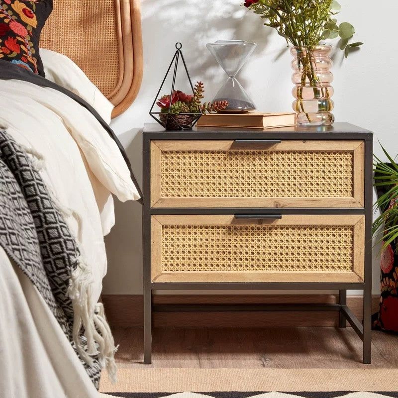 Two-drawer nightstand with wicker design and black frame next to a bed.