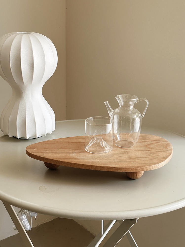 Clear glass pitcher and cup on a wooden tray with a white decorative object in the background.