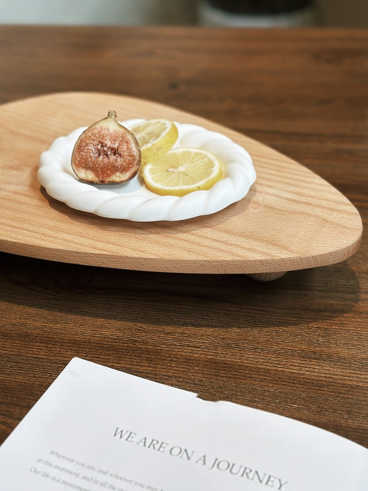 Wooden plate with fig, lemon, and white cheese on a wooden table with a book in the foreground.