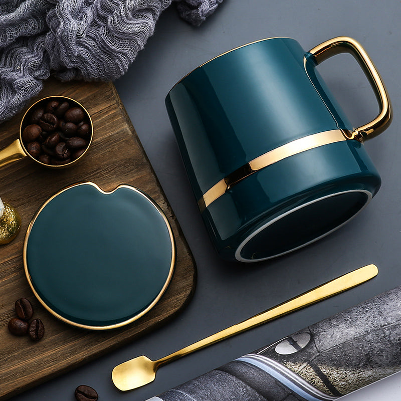 Teal mug with gold accents on a dark surface with coffee beans and a spoon.