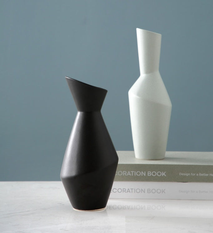 Two vases, one black and one white, on a surface with a gray background.