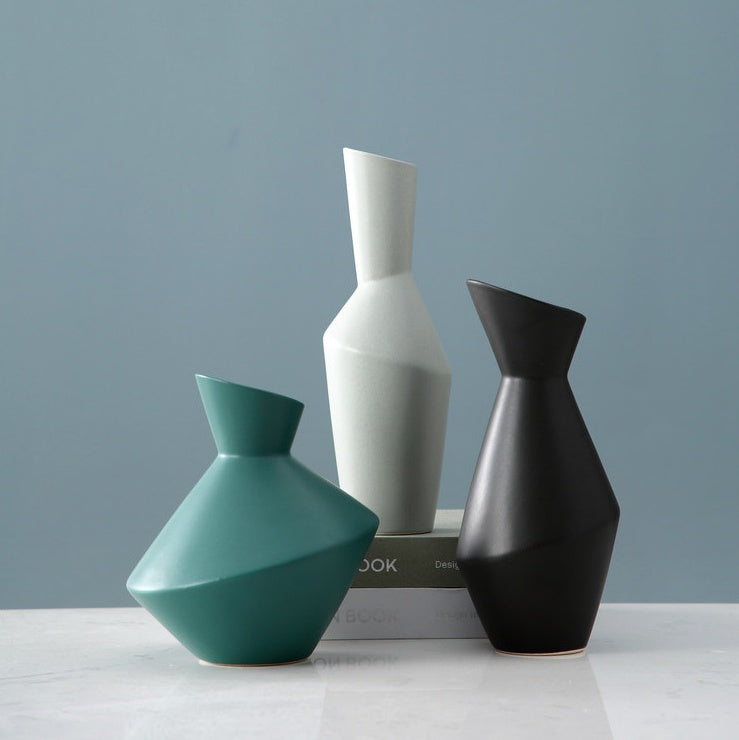 Three geometrically shaped vases in teal, gray, and black on a light surface with a gray background.