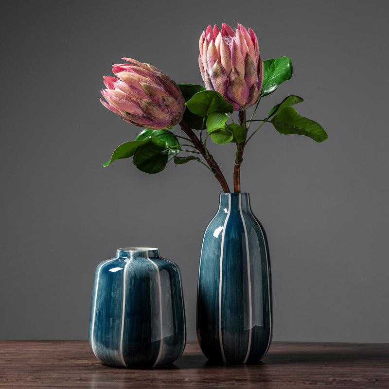 Two blue vases with flowers on a wooden surface against a gray background