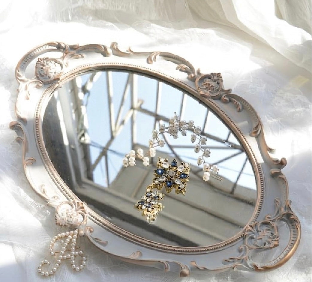 Decorative mirror with ornate frame reflecting jewelry on a white fabric background