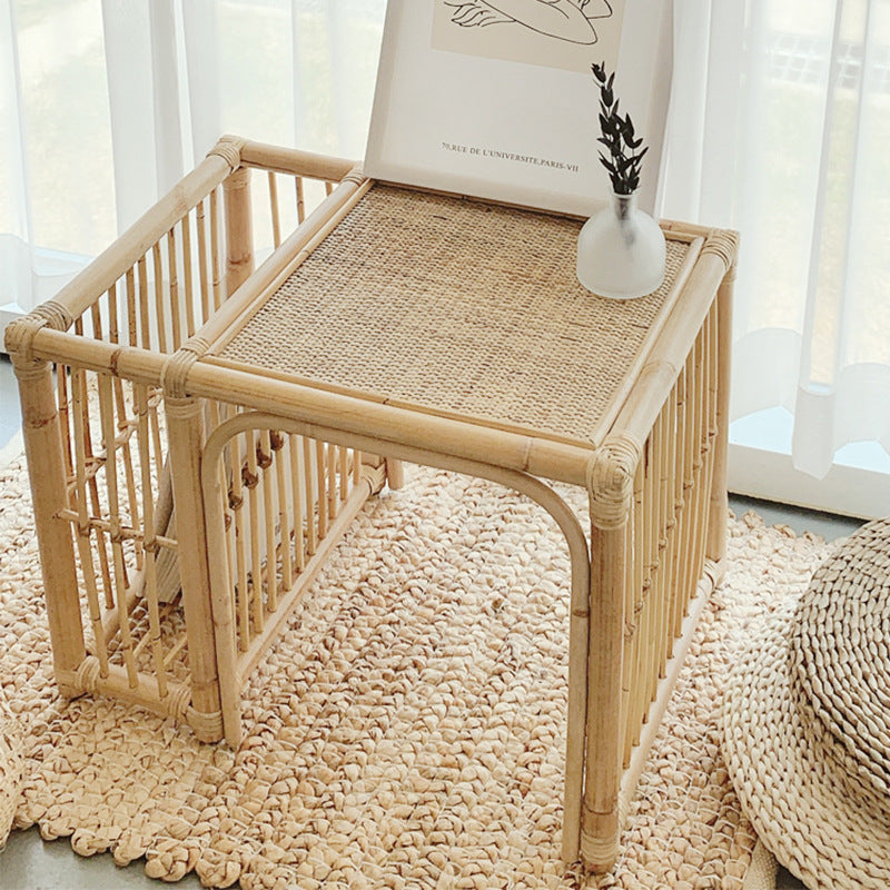 Rattan side table with a vase and plant in a room with light curtains.