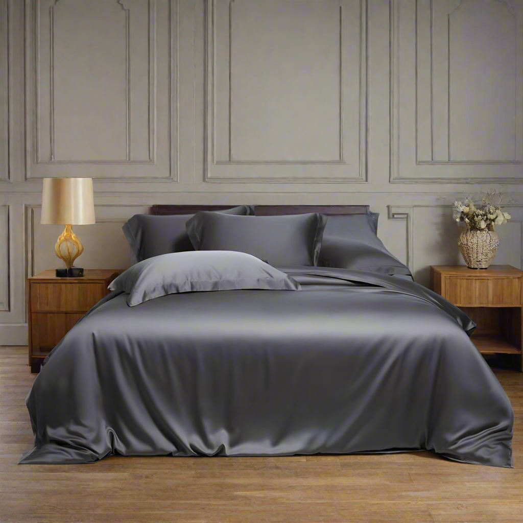 Gray satin bedding set on a bed in a bedroom with wooden nightstands and a lamp.