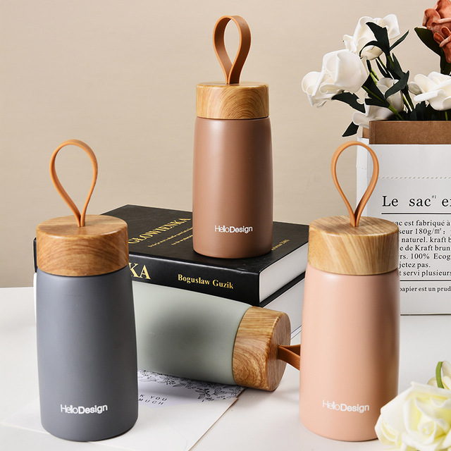 Set of three insulated bottles with wooden lids on a surface with books and flowers in the background.