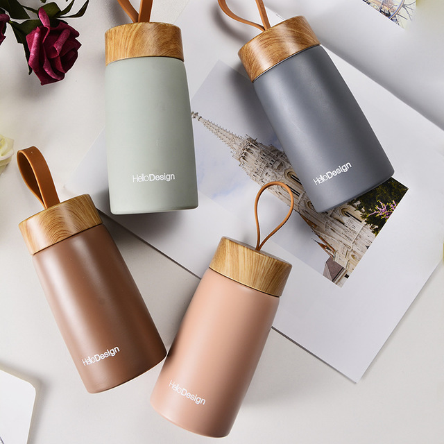 Four insulated cups with wooden lids on a surface with a magazine underneath.