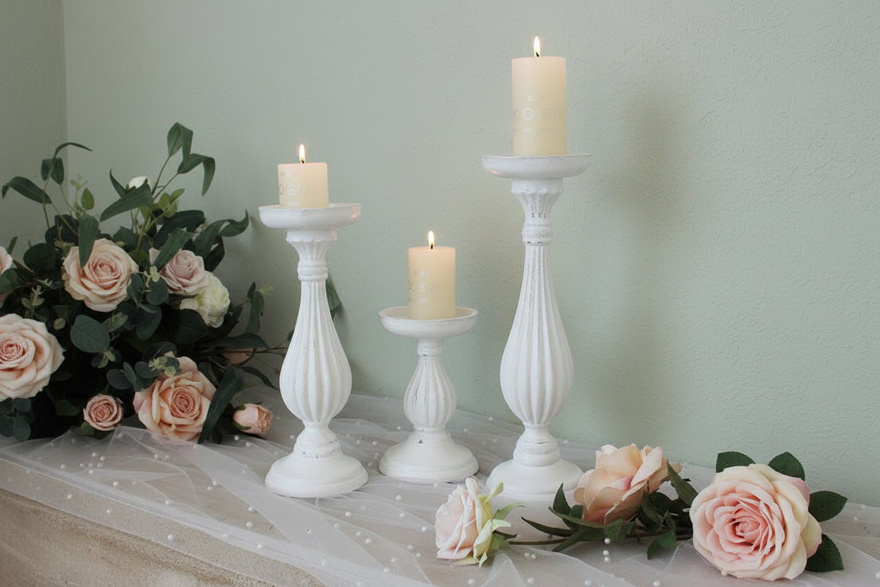 Three white candle holders with candles on a decorative surface with flowers.