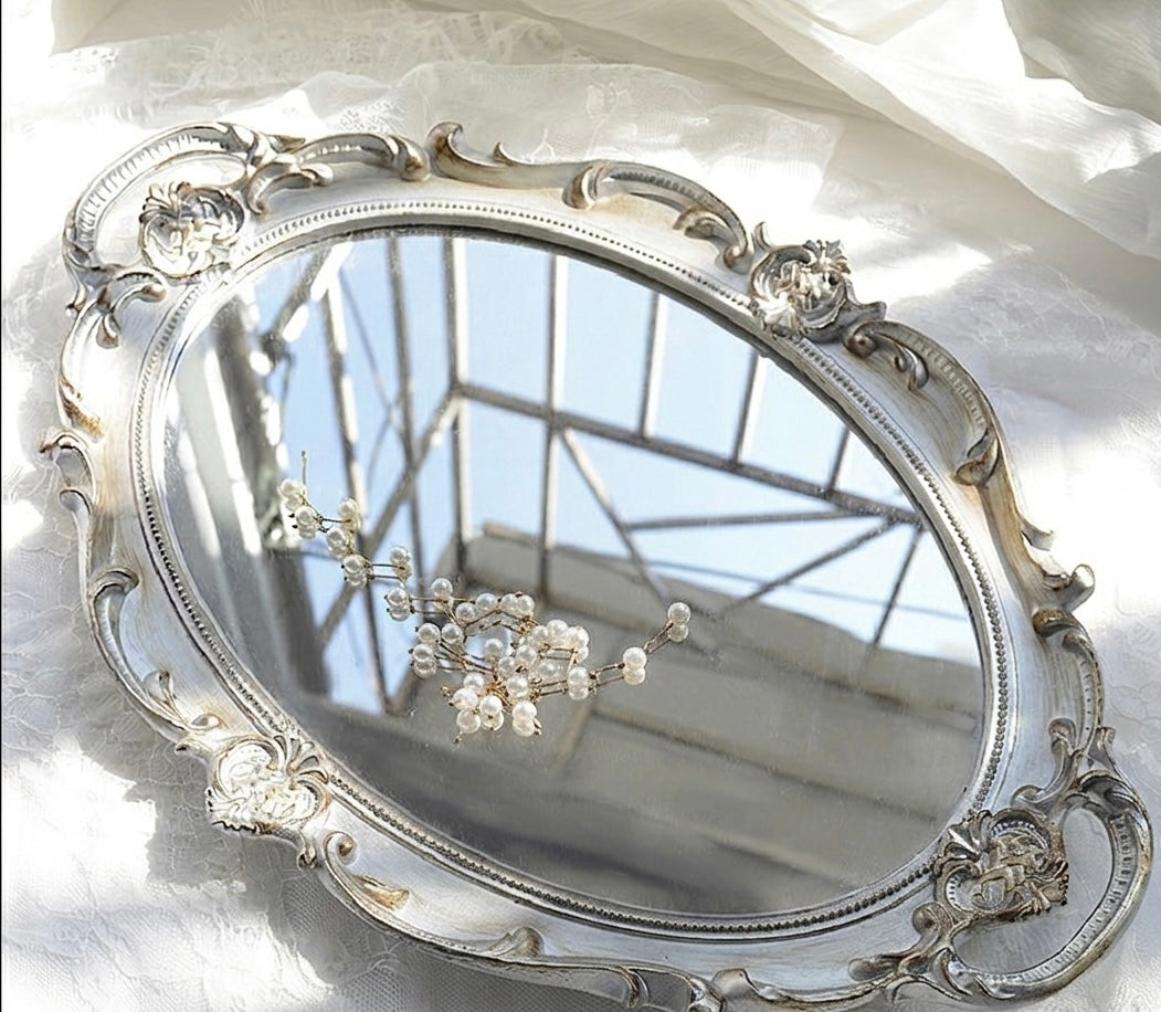 Decorative silver mirror with intricate designs on a white background