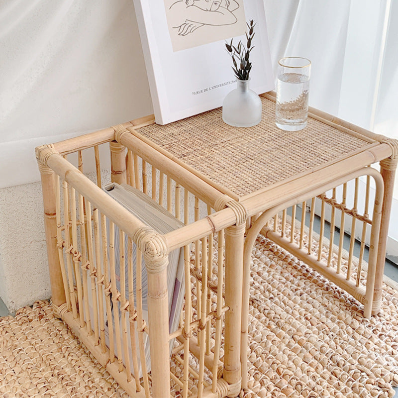 Rattan side table with a glass of water and a plant in a minimalistic room.