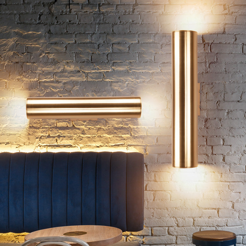 Gold cylindrical wall lights on a stone wall with a blue cushioned bench.