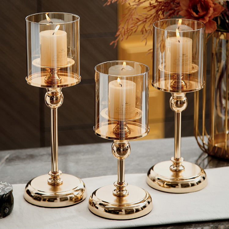 Three gold candle holders with clear glass covers on a marble surface.