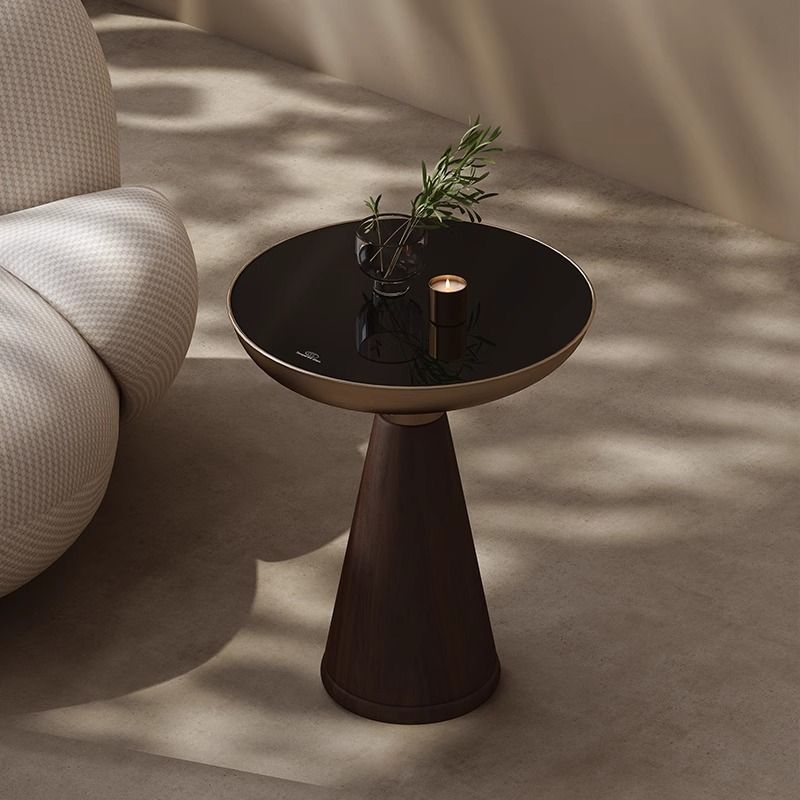 Small black side table with a plant and candle next to a beige armchair on a neutral background