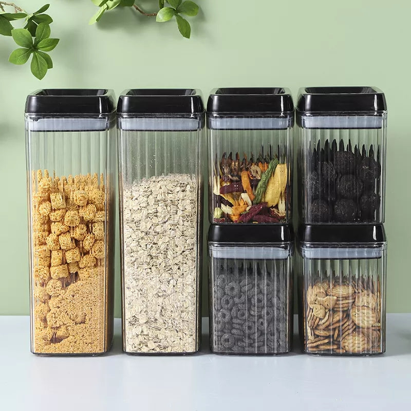 Set of six transparent storage containers with black lids, each filled with different food items on a light green background.
