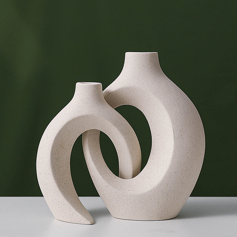 Two beige ceramic vases with a unique design on a white surface against a dark green background
