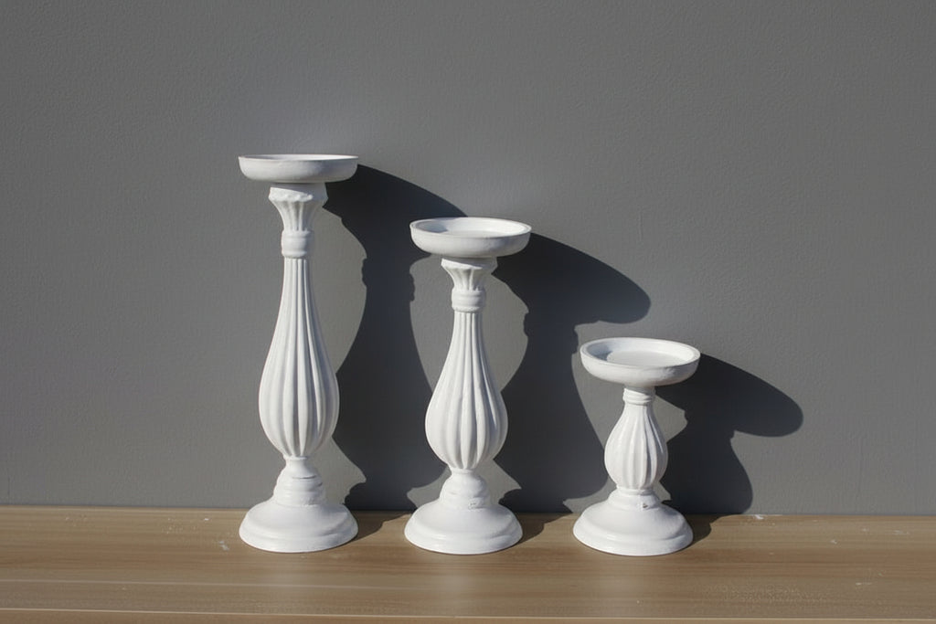 Three white decorative candle holders of different sizes on a wooden surface with a gray background
