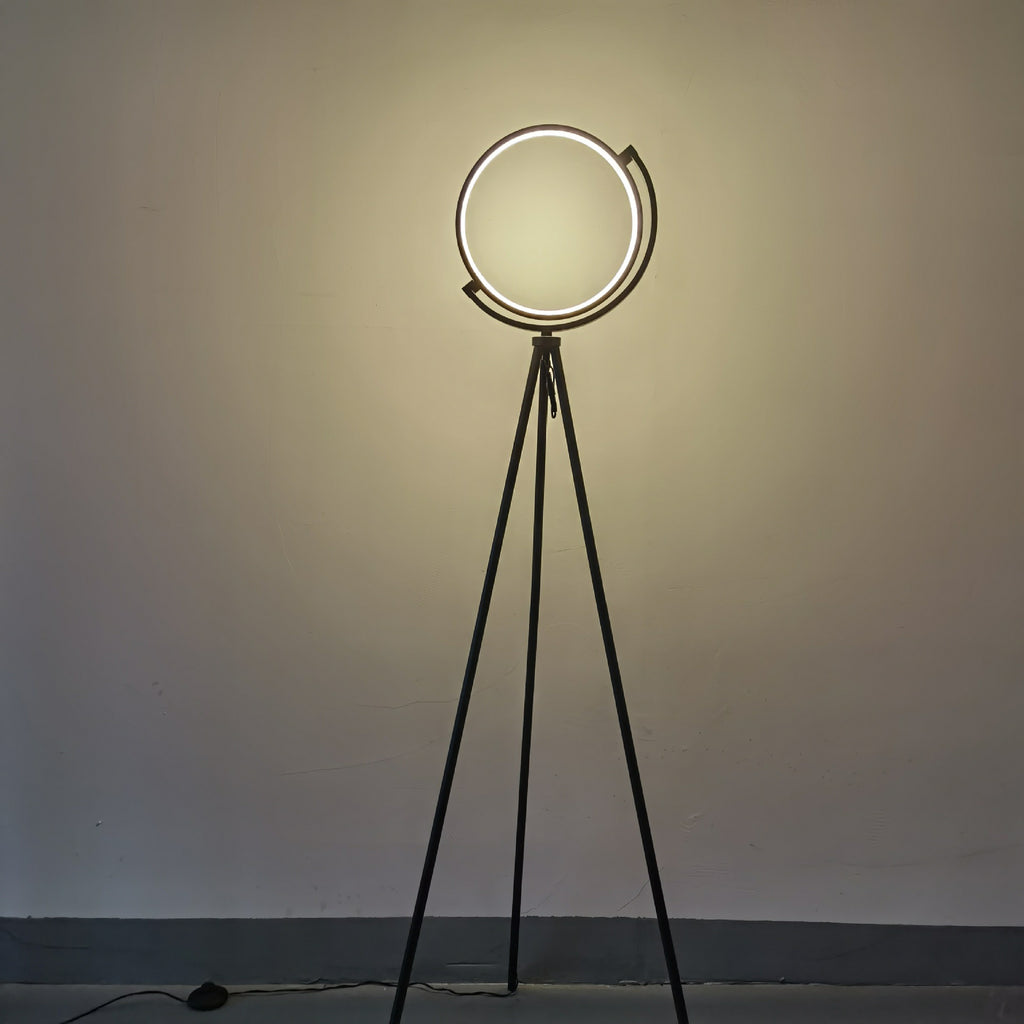 Floor lamp with circular design on a tripod stand against a plain wall.