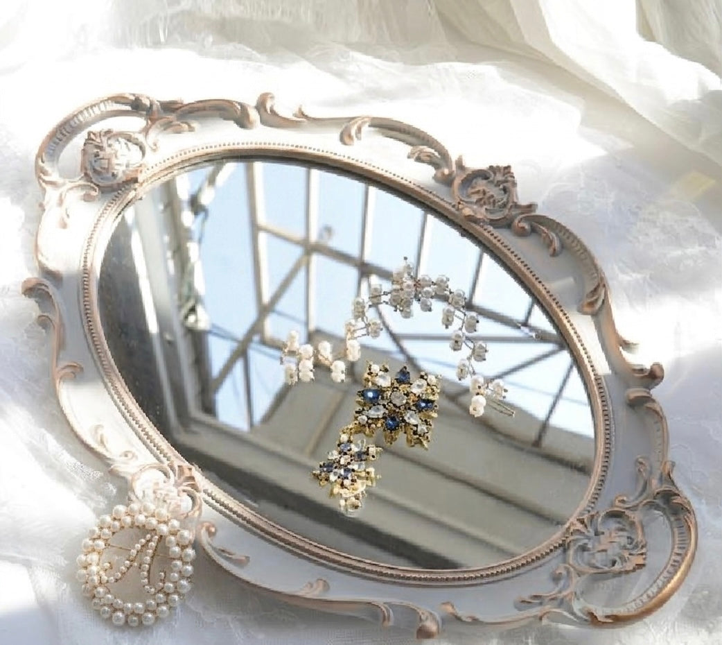 Decorative mirror with ornate frame on a white surface, reflecting a window.