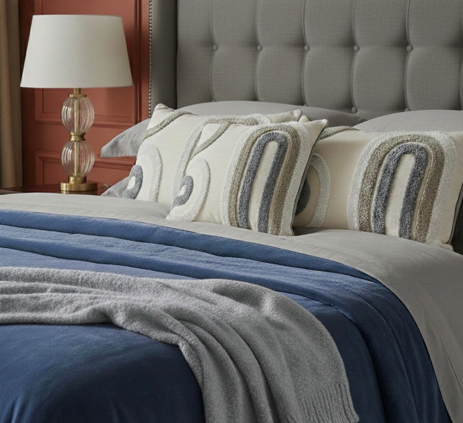 Neatly made bed with decorative pillows and a lamp on a bedside table.