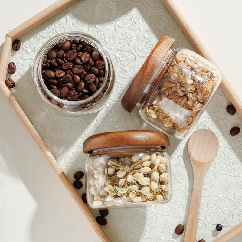 Three glass jars with wooden lids containing coffee beans and grains on a textured surface.
