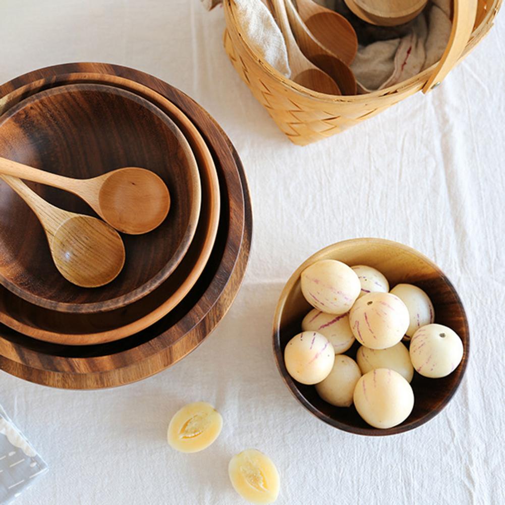 Wooden bowls and spoons on a white surface with a basket of additional items.