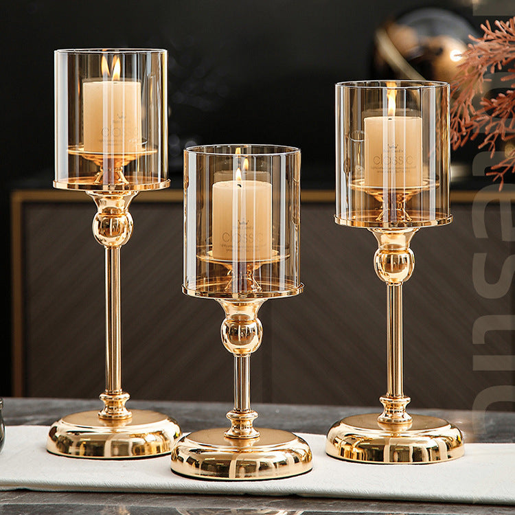 Three gold candle holders with clear glass covers on a marble surface.